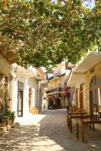 Cobblestone street lined with cafes, shops, and trees with string lights in a quaint town.