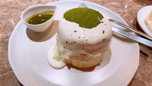 A round matcha tiramisu with a creamy white top, dusted with green matcha powder on a plate.