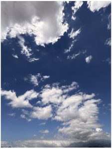 A bright blue sky filled with varying white clouds, some fluffy and others wispy, creating a dynamic and serene atmosphere.