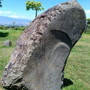 
A large, standing stone with a rough, textured surface partially displaying a carved design.