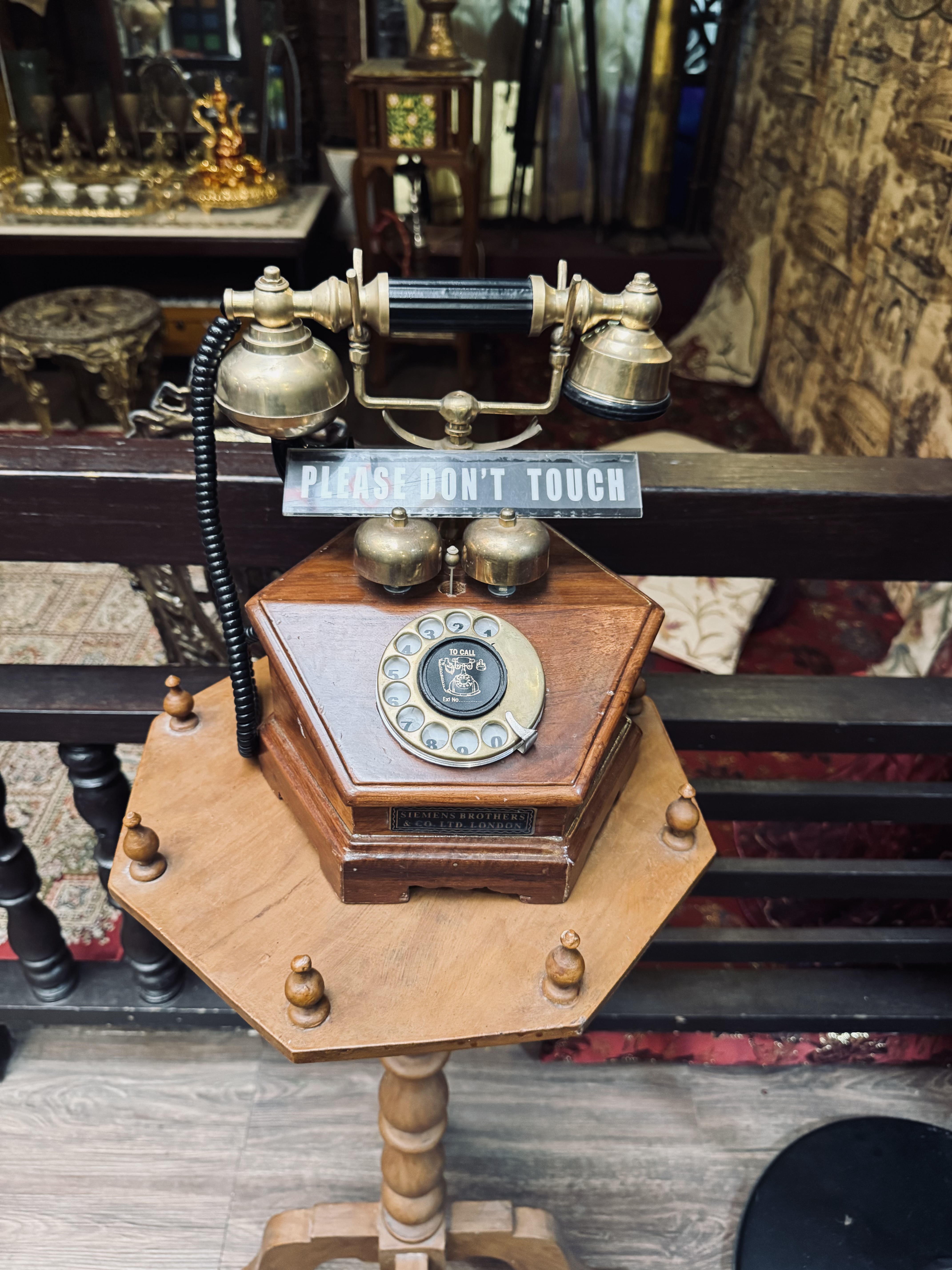 An antique telephone sits on an octagonal wooden pedestal.