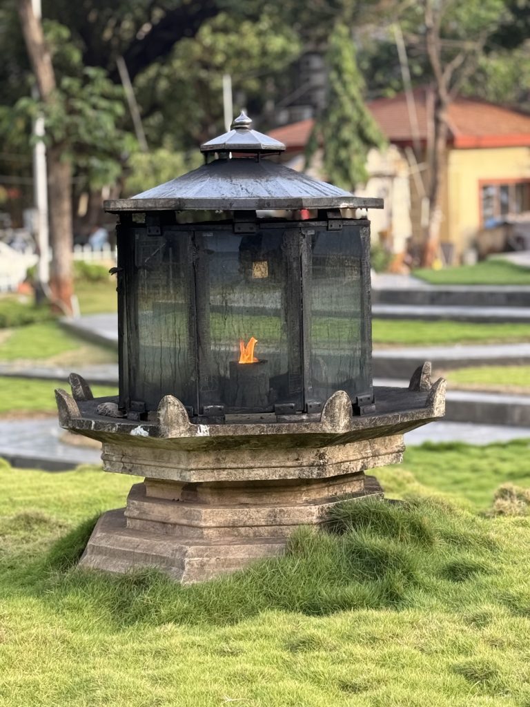 A circular stone structure with a thatched roof, featuring a transparent enclosure that has a flickering flame inside.