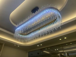 Modern chandelier with cascading blue and green LED lights hangs from a coffered ceiling, creating an elegant and sophisticated atmosphere.