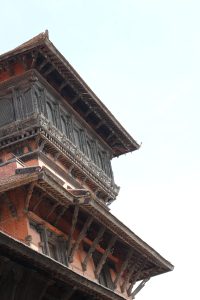 Close-up of a Nepalese pagoda with detailed wood carvings and tiered roofs under a clear sky, showing its historic beauty.