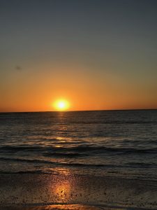 A tranquil sunset over the ocean, with the sun sinking just above the horizon, casting a warm golden glow across the water