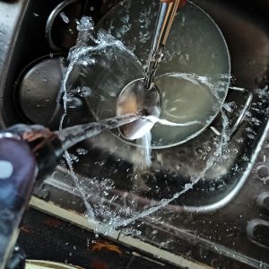 
A close-up view of a kitchen sink with water flowing from two faucets into a bowl.