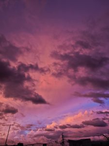 A dramatic sunset sky filled with deep pink and purple clouds over a quiet city scene, with silhouettes of rooftops and power lines in the foreground