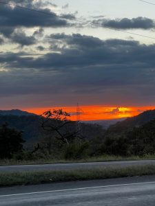 Sunset over mountains with dark clouds and a silhouetted transmission tower.