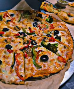 A freshly baked pizza topped with a variety of colorful vegetables, including sliced black olives, red and green bell peppers, mushrooms, and broccoli, all melted under a layer of bubbling cheese
