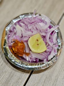 Fresh chopped onions with a slice of lemon and pickle served on a small plate. A simple side dish shot in Kurla, Mumbai. 
