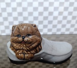 Adorno muy antiguo de un gato con mucho pelaje de color café dentro de un zapato formal de color gris.