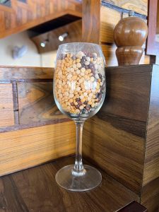 A wine glass filled with layers of various colorful dried beans and lentils, sitting on a wooden surface.