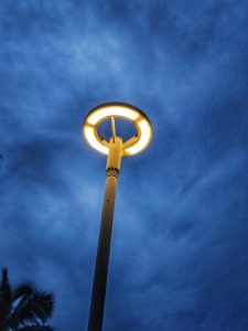 A tall street lamp with a circular light glowing against a deep blue evening sky.
