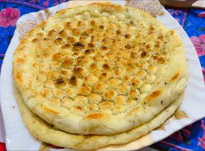 A plate with two pieces of golden brown naan, slightly puffed and sprinkled with sesame seeds.
