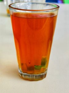 A close-up of a glass of amber lime tea with mint leaves at the bottom.