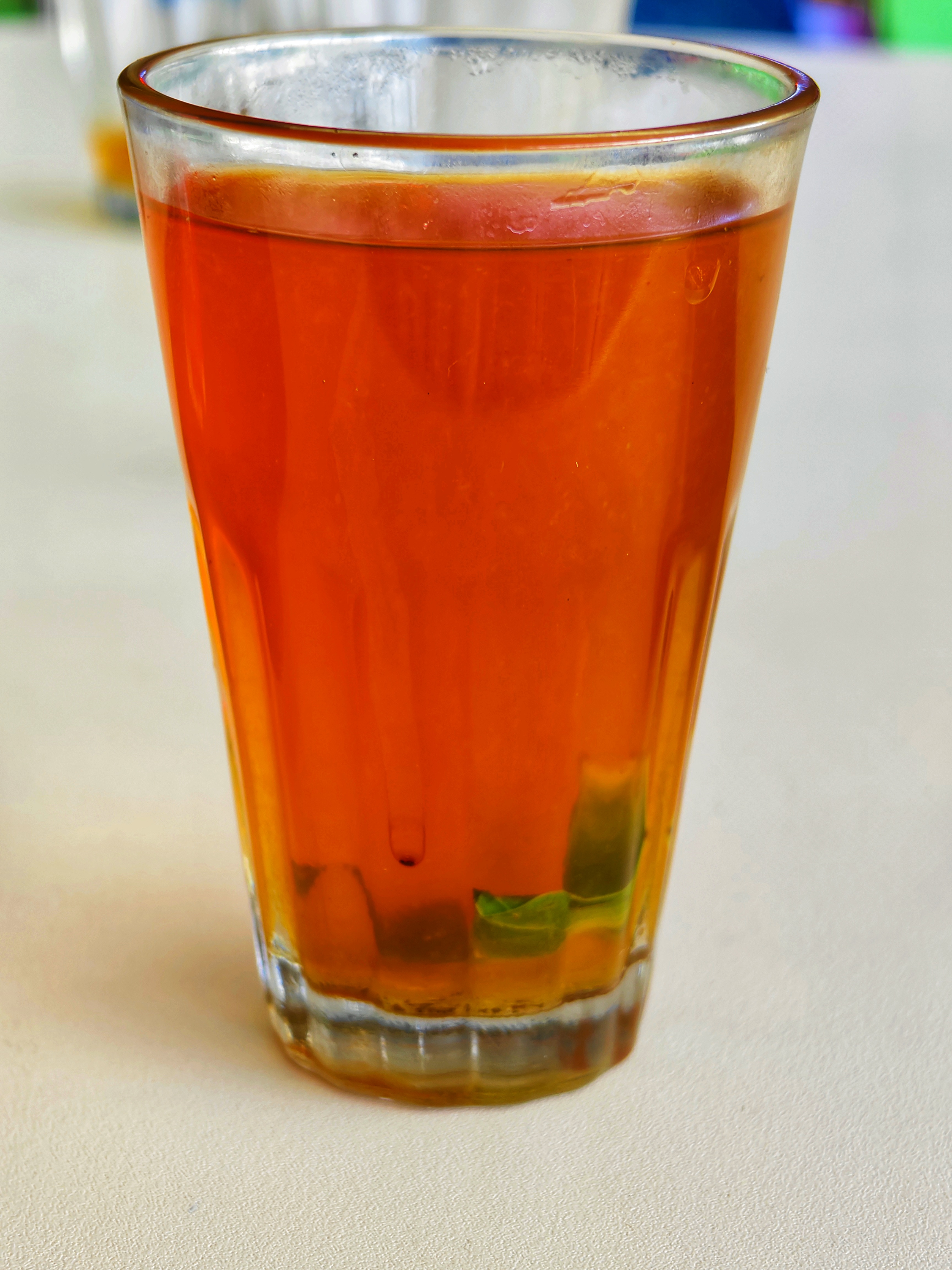A close-up of a glass of amber lime tea with mint leaves at the bottom.