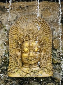 Golden deity face carving on stone with flowing water, creating a calm and serene scene.