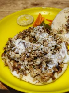 A close-up of shawarma on a yellow plate, topped with shredded grilled meat and creamy sauce.