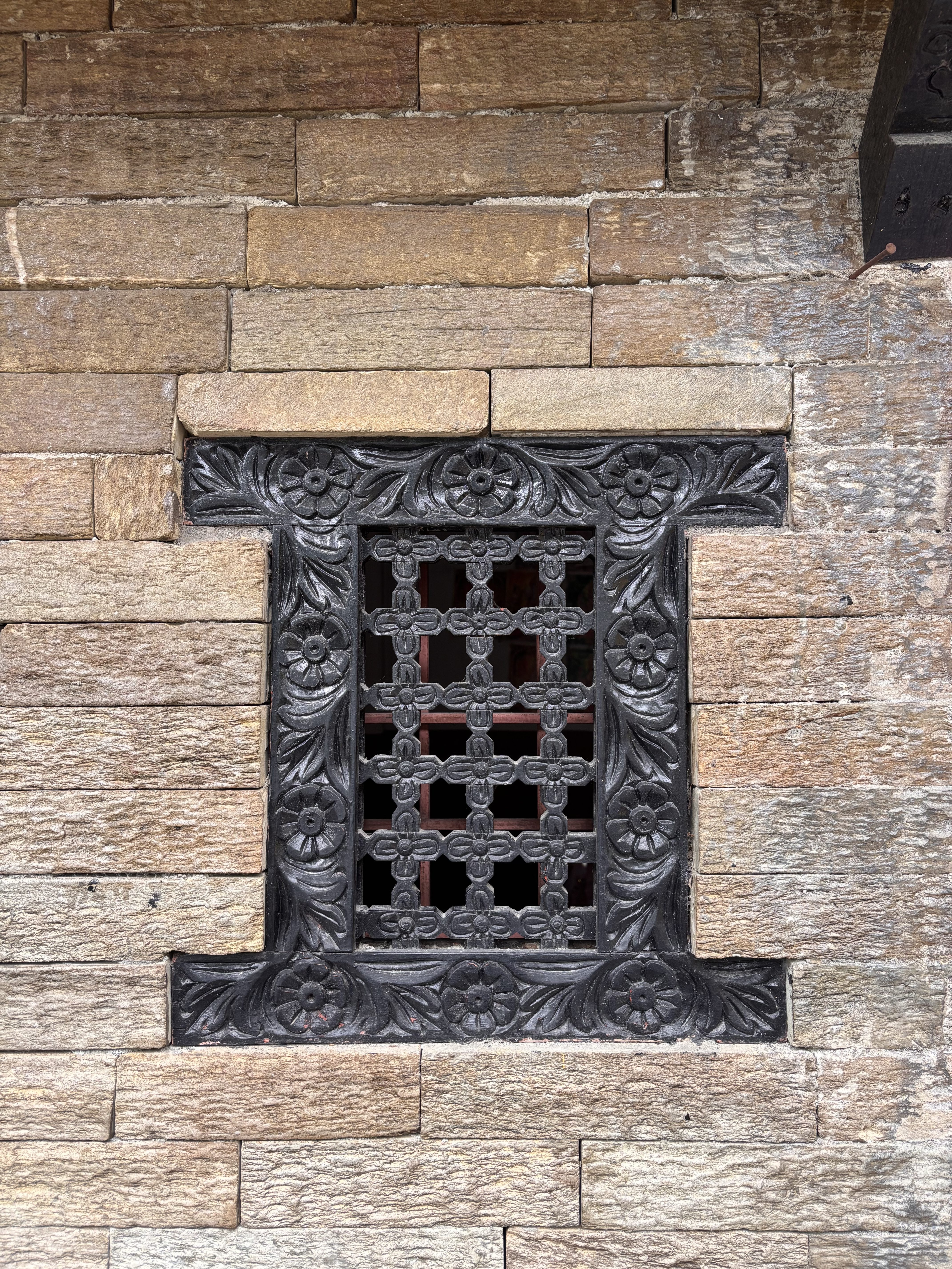 Ornate black metal grate with floral patterns set into a rustic wall.