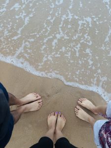 A picture of three people’s feet in the sandy land near the sea.
