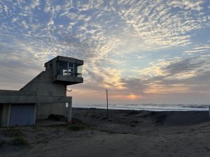 

A modern, angular building with a glass observation area is positioned on sandy terrain near the Toyoumi Coast beach.