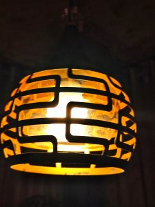 A close-up of a stylish pendant lamp with a yellow glass globe inside a black geometric metal frame.