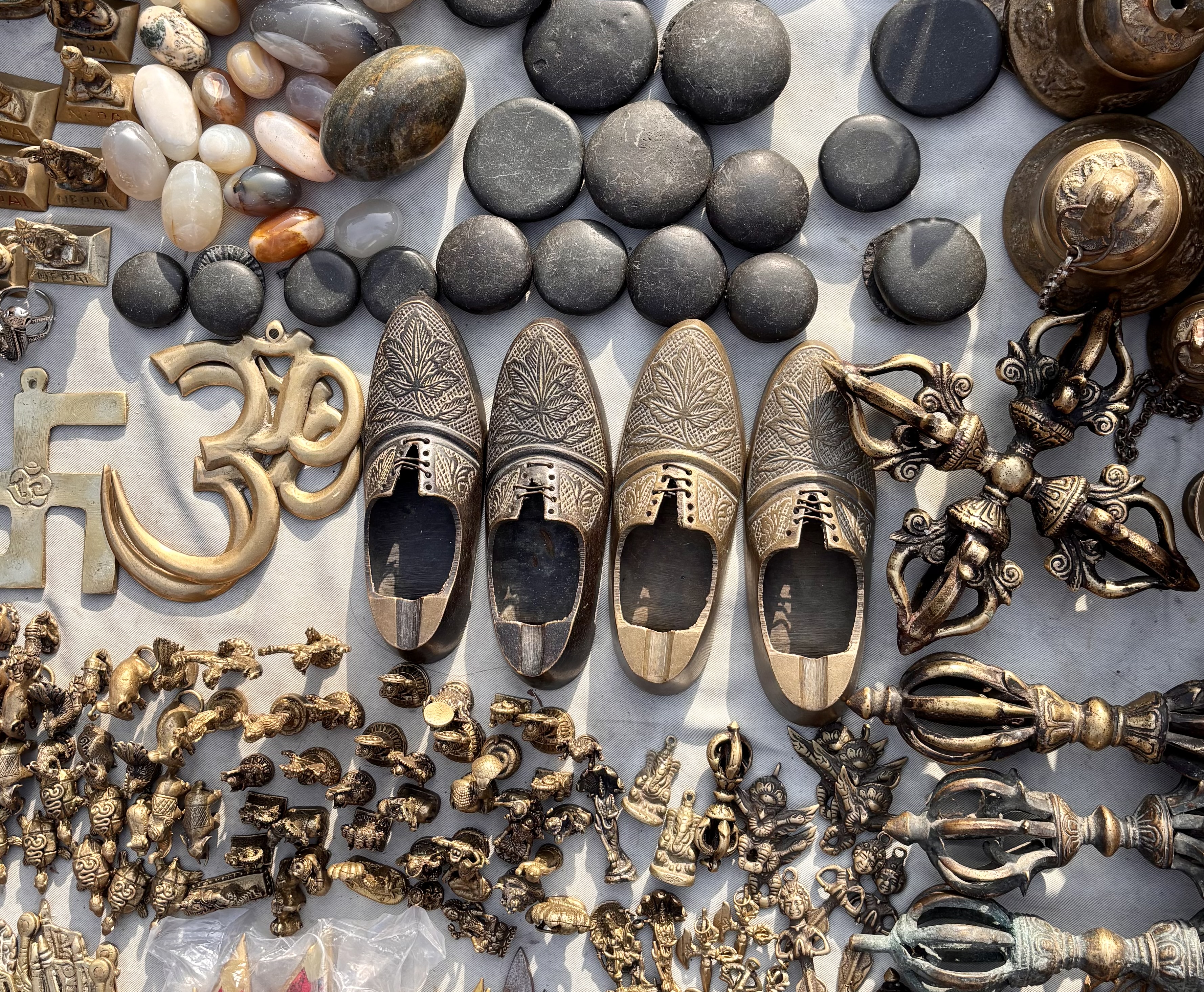 A display featuring carved metal shoes, a brass Om symbol, black stones, and intricate metal sculptures.
