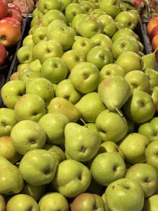 A pile of fresh green pears is displayed, with bright red apples partially visible on the left