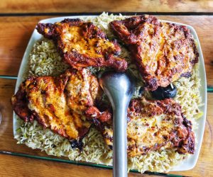 Grilled chicken thighs with a golden crust atop a bed of seasoned rice on a square white platter.