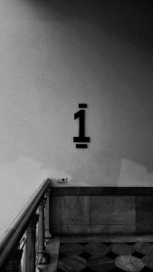 A black and white image features a wall with the number "1" prominently displayed in a bold, dark font.