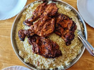 A silver serving platter holds a generous portion of fluffy white rice topped with several pieces of well-grilled chicken. 