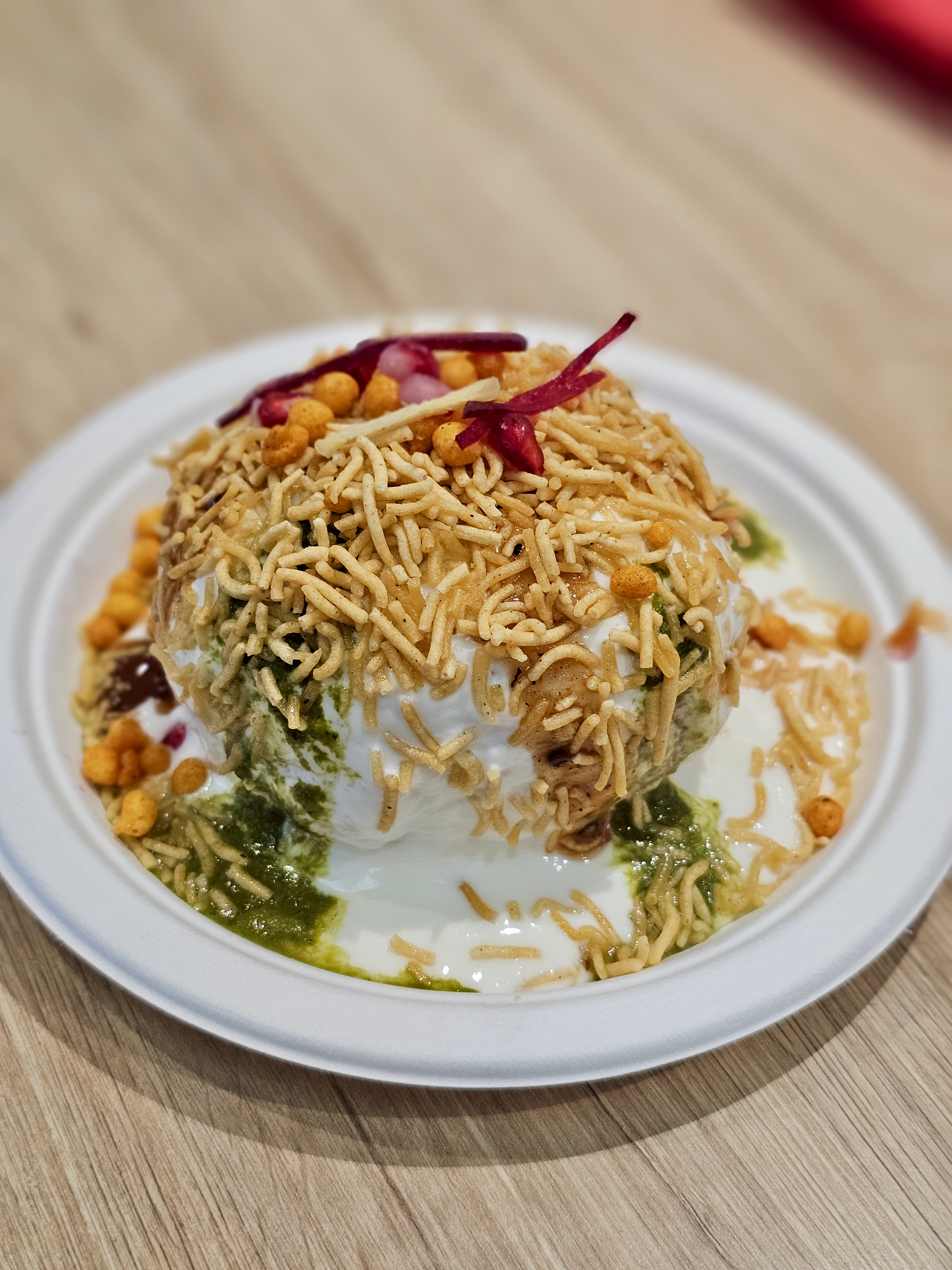 A delicious plate of chaat (Dal Kachori) topped with sev, curd, chutneys, and pomegranate looks rich in flavor and texture. Captured at a food spot in Kurla, Mumbai.