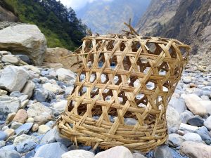 Woven basket on a rocky riverbed with lush trees and misty mountains in the background.