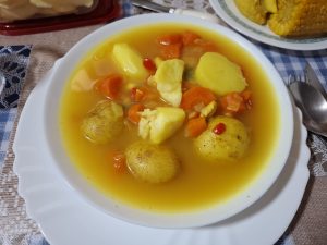 Soup with potatoes and sliced carrots. The soup is on a white bowl, which is on top of a white plate.