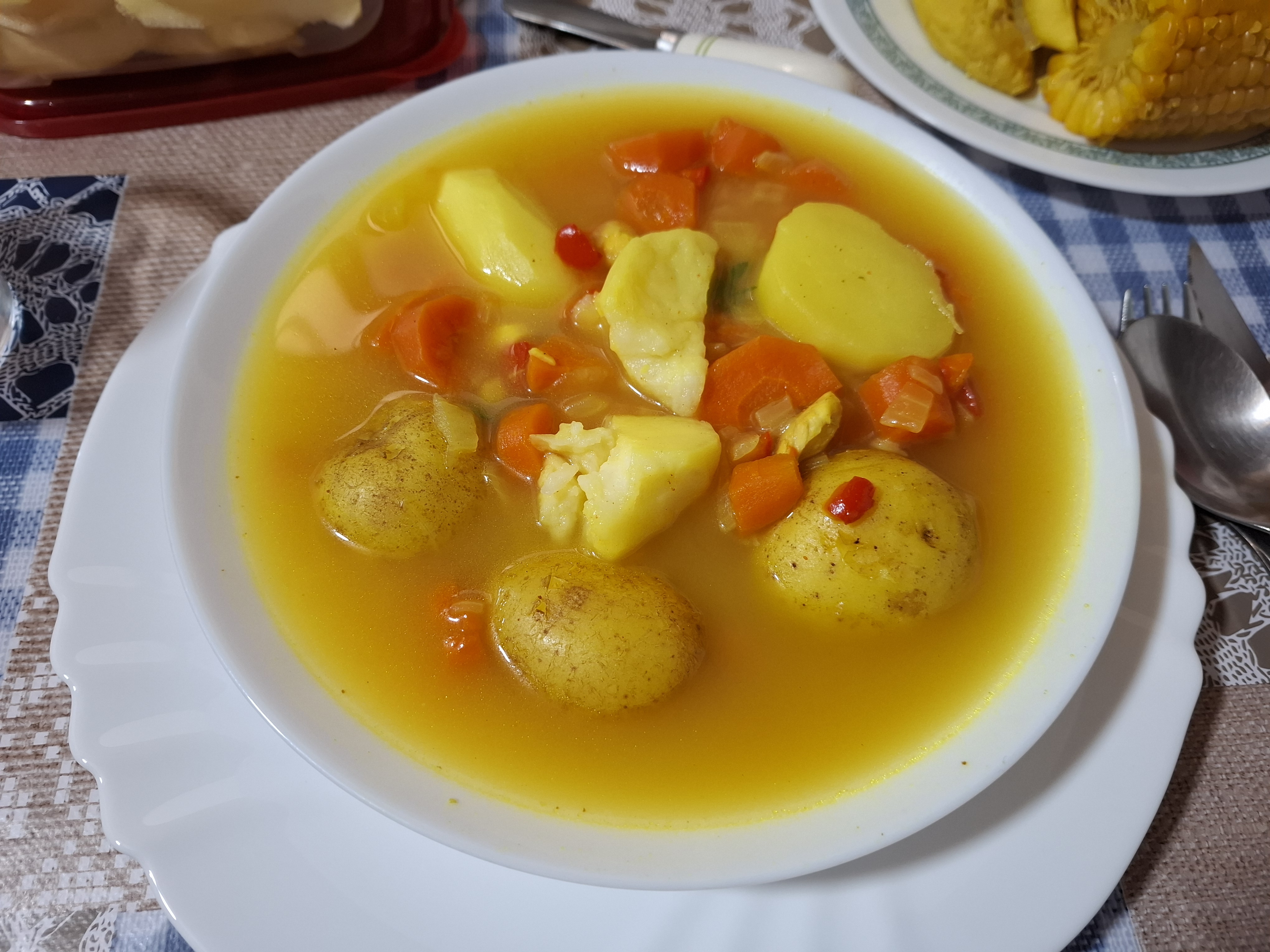 Soup with potatoes and sliced carrots. The soup is on a white bowl, which is on top of a white plate.