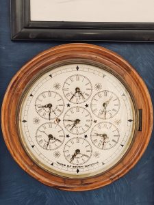This elegant wooden wall clock displays the time of seven different cities around the world. The antique-style design, detailed mini dials, and soft indoor lighting create a classic and artistic atmosphere. Captured indoors in Kurla, Mumbai.