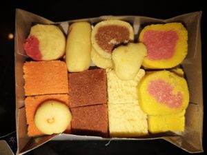 A box filled with colorful assorted sweets in various shapes and textures, including pink, yellow, orange squares and round pieces, conveying a festive mood.