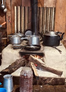 Rustic kitchen with metal pots and a black kettle on a clay stove fueled by wood logs.
