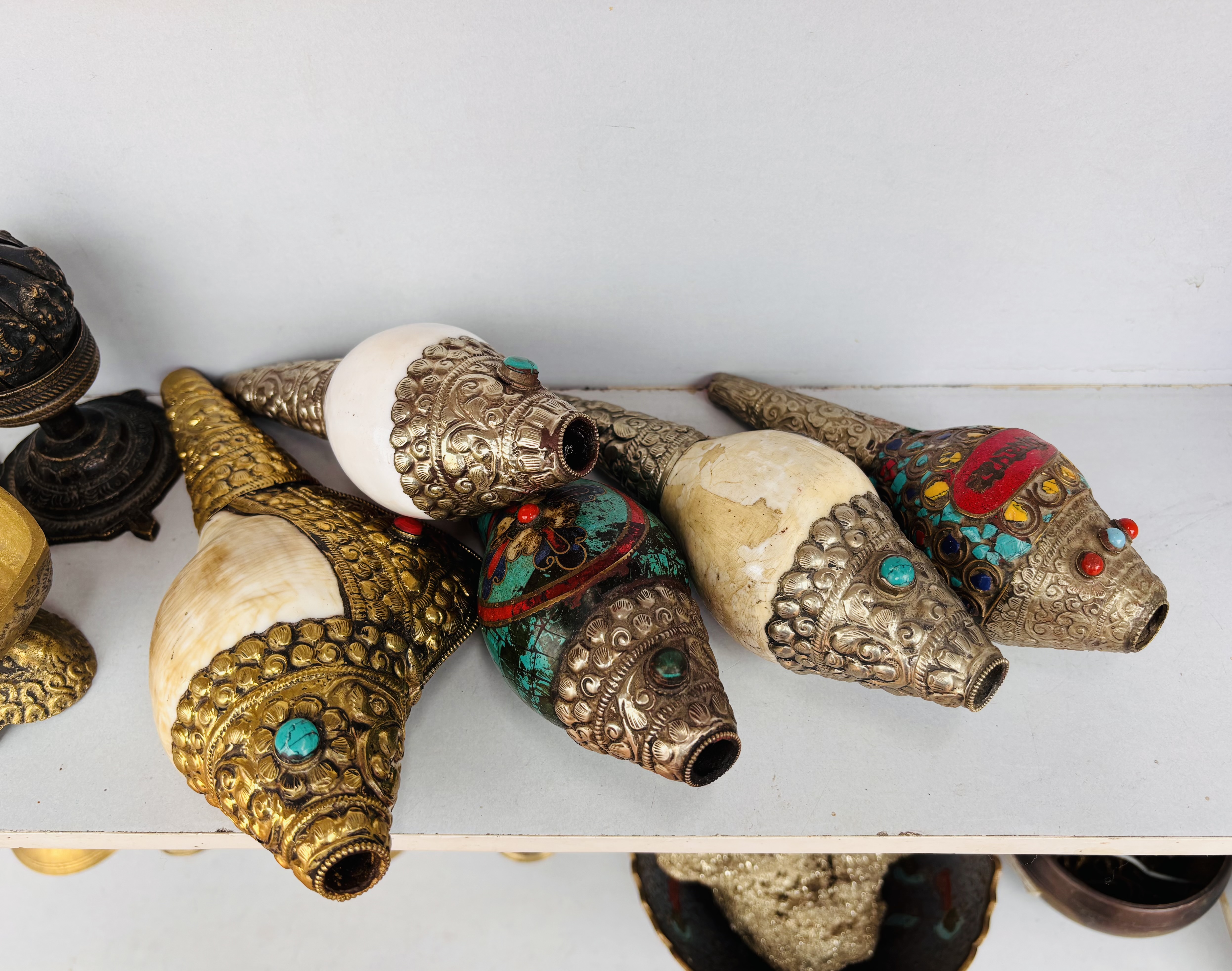 Intricately decorated conch shells resting on a white shelf, adorned with ornate metalwork and turquoise, red, and gold accents.