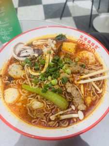 Hotpot noodles (Malatang) in a large bowl with mushrooms, vegetables, meat, chicken broth, and chilies.
