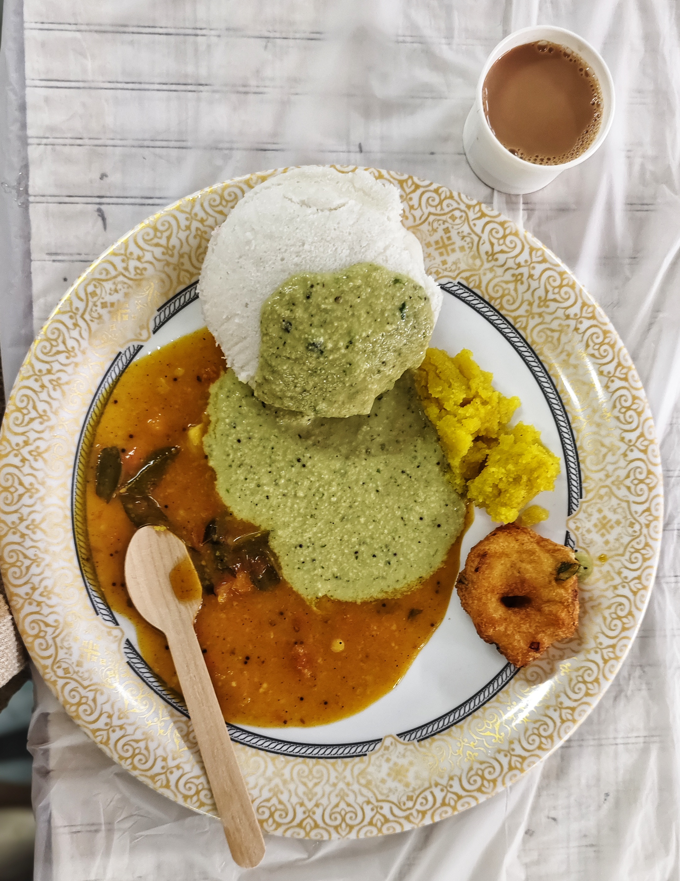 A round plate with a golden border holds South Indian breakfast of idlis topped with green chutney.