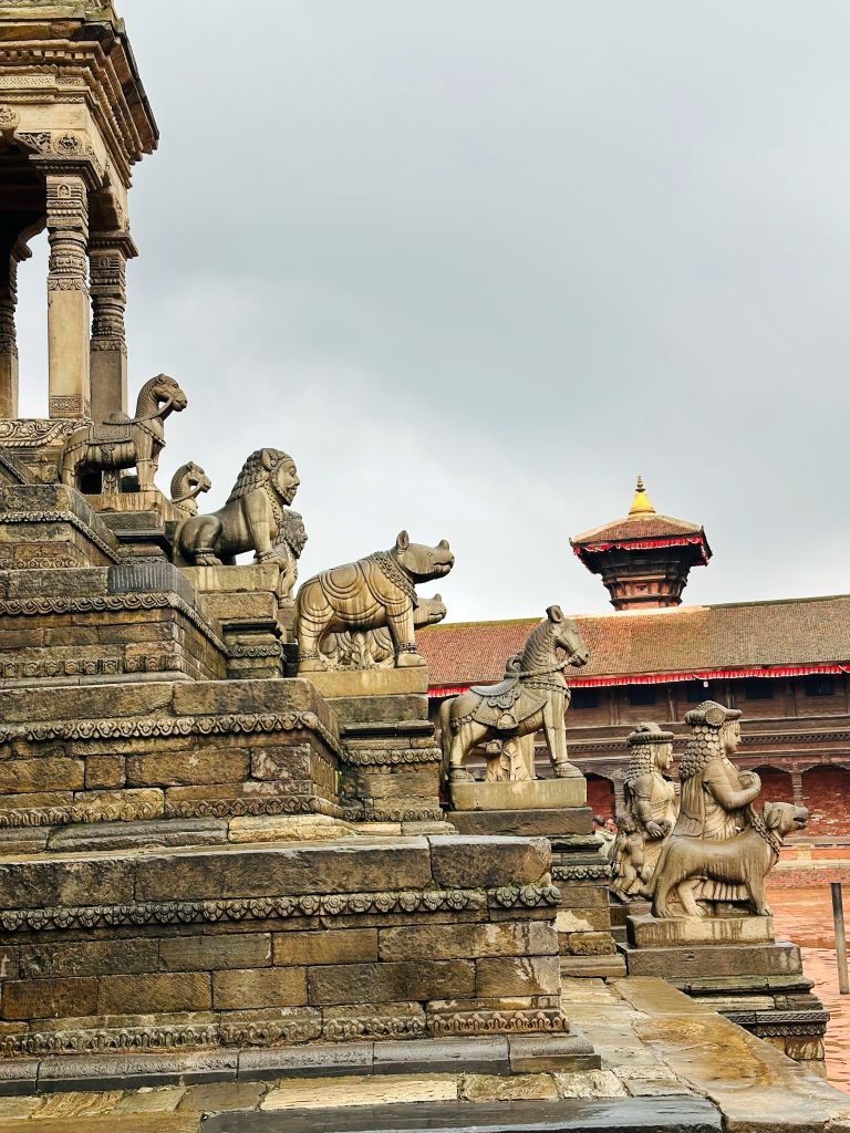 Ancient stone temple staircase adorned with animal sculptures, including lions and rhinos, leading to pagoda-style building under overcast sky.