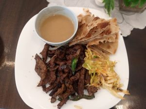 A plate with chapati, cooked meat, shredded vegetables, and a small bowl of vegetable sauce.