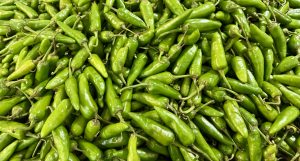 A close-up of a large pile of bright green chili peppers in varying sizes and shapes, creating a fresh and vibrant texture.