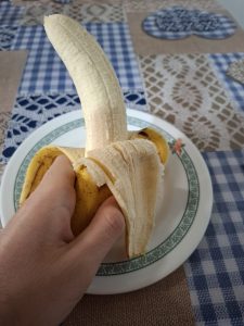 A hand holding a peeled banana, with a plate underneath.