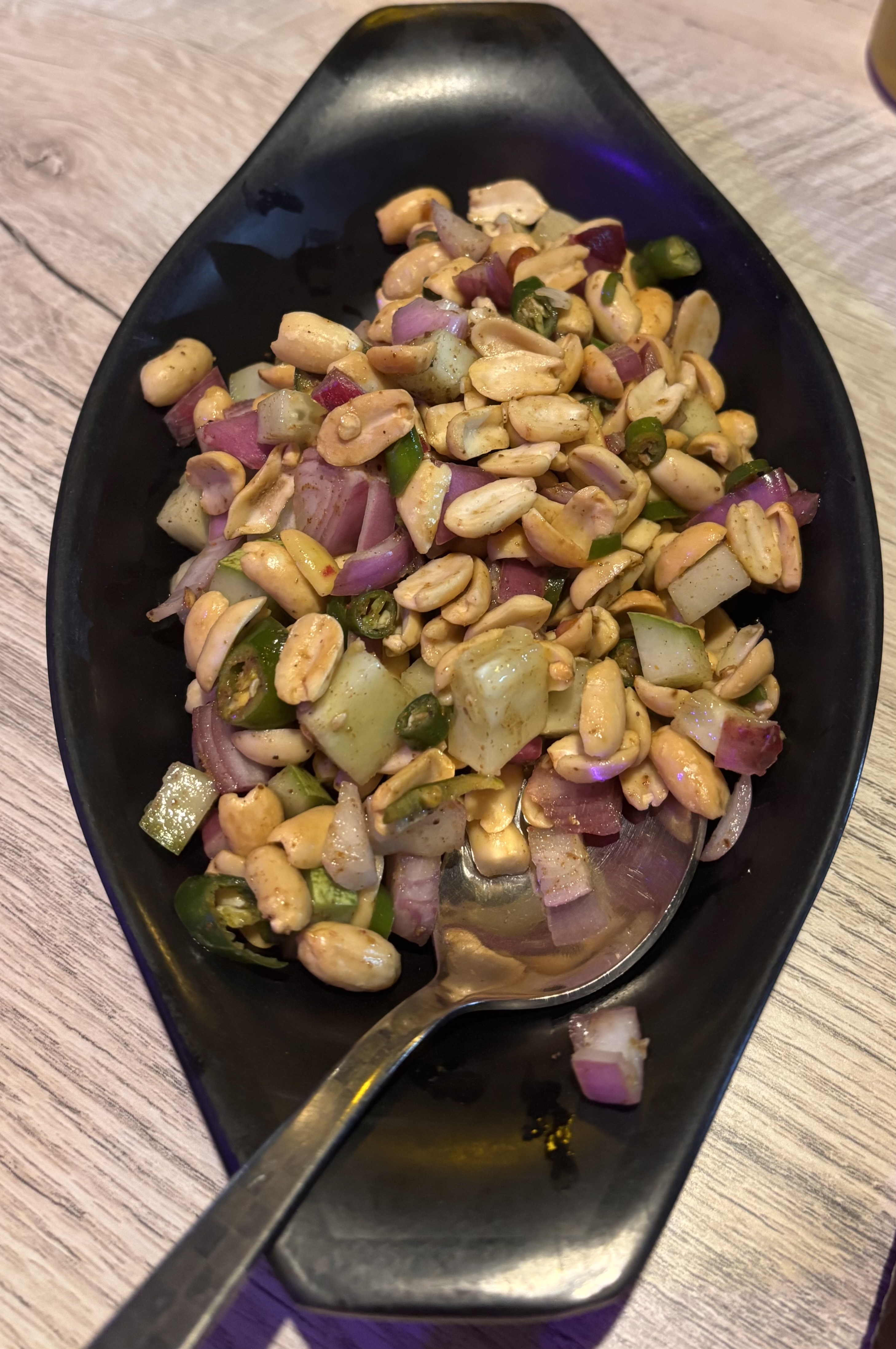 Spicy peanut salad with chopped red onions, green chilies, and cucumber served in a black bowl with a spoon on a wooden table.