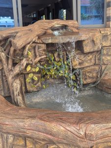 A decorative fountain with cascading water, featuring faux stone and wood elements, decorated with artificial leaves.
