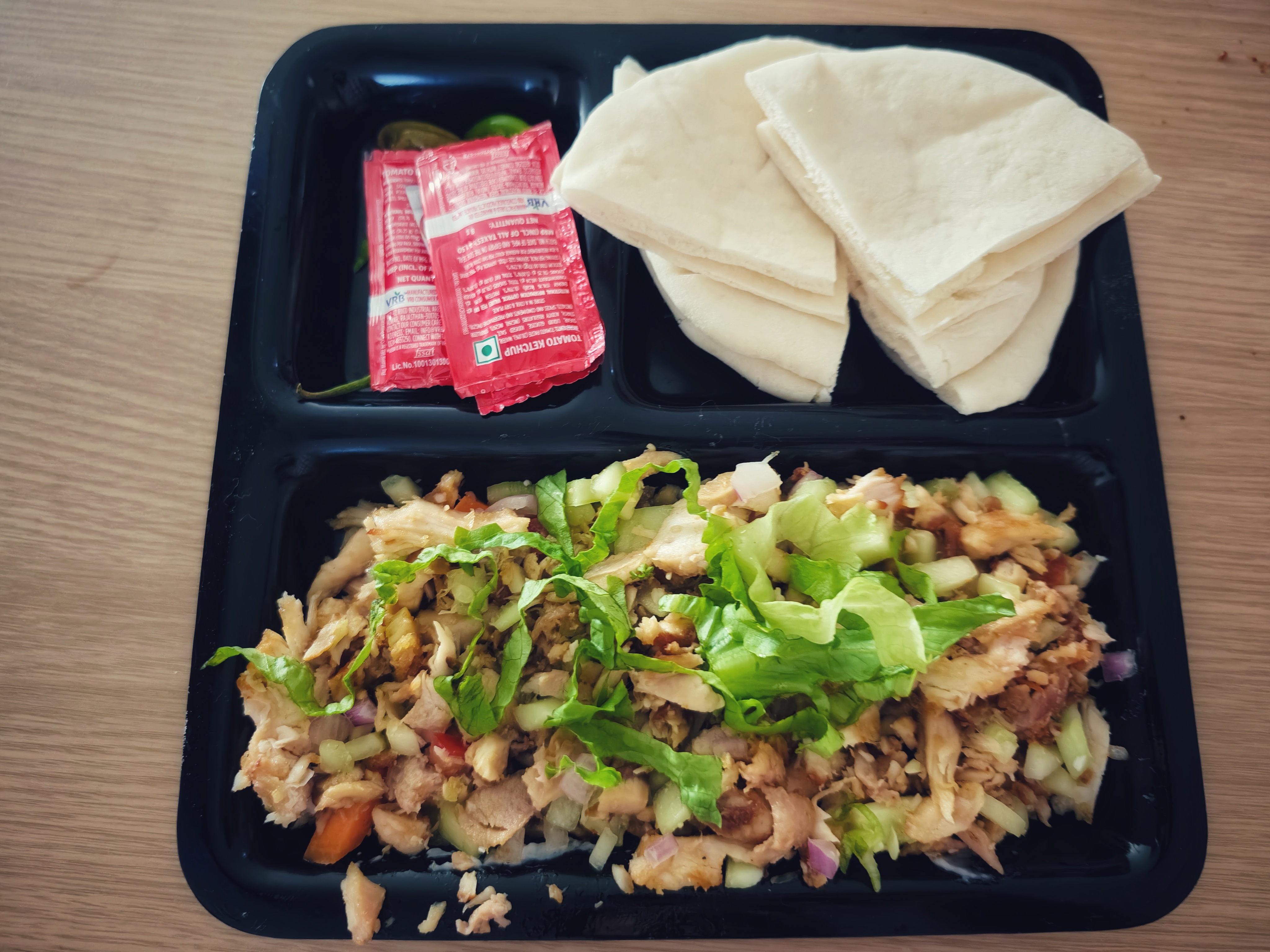 A black tray of chopped chicken shawarma with diced vegetables, topped with shredded lettuce.