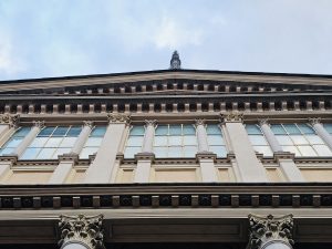 An upward view of a detailed historic building (Mole Antonelliana) highlights elegant columns, windows, and symmetry against the soft, cloudy sky in Turin (Torino), Italy.