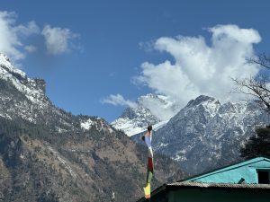 Snow capped mountains under a blue sky with clouds and a colorful flag on a turquoise roof.